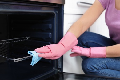 Woman cleaning oven rack with rag in kitchen, closeup