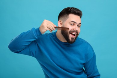 Photo of Handsome young man combing beard on light blue background