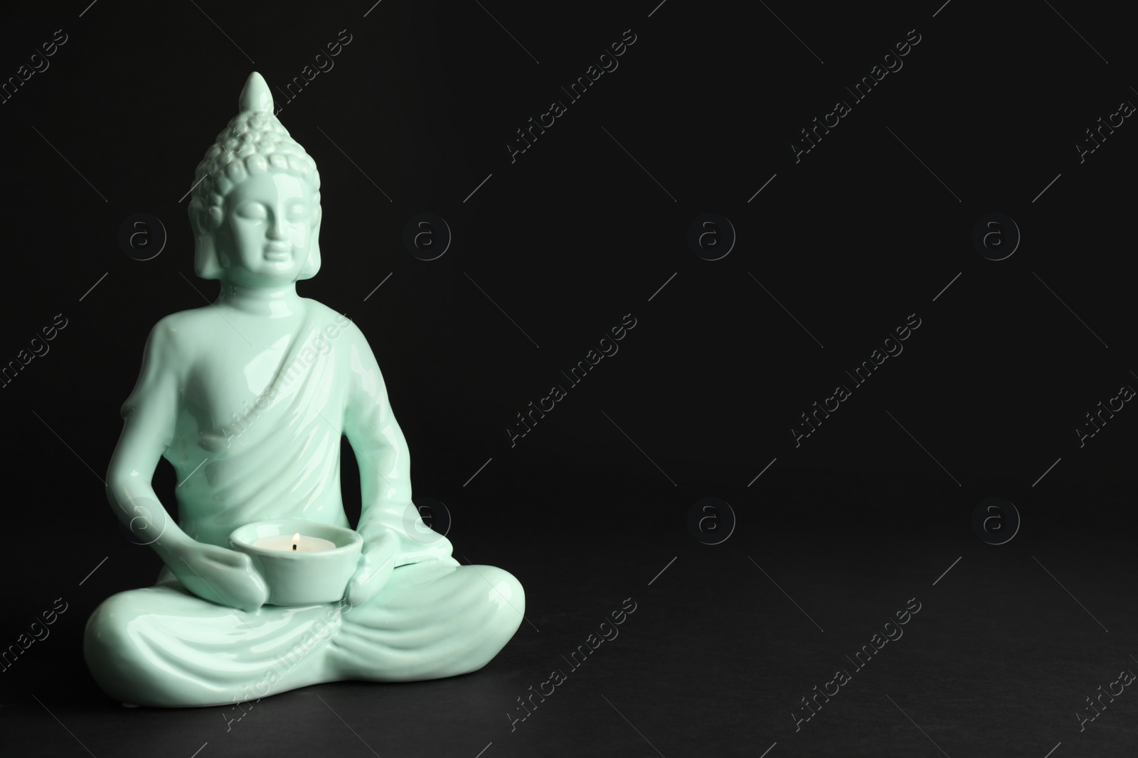 Photo of Beautiful ceramic Buddha sculpture with burning candle on black background. Space for text