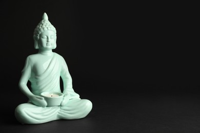 Photo of Beautiful ceramic Buddha sculpture with burning candle on black background. Space for text