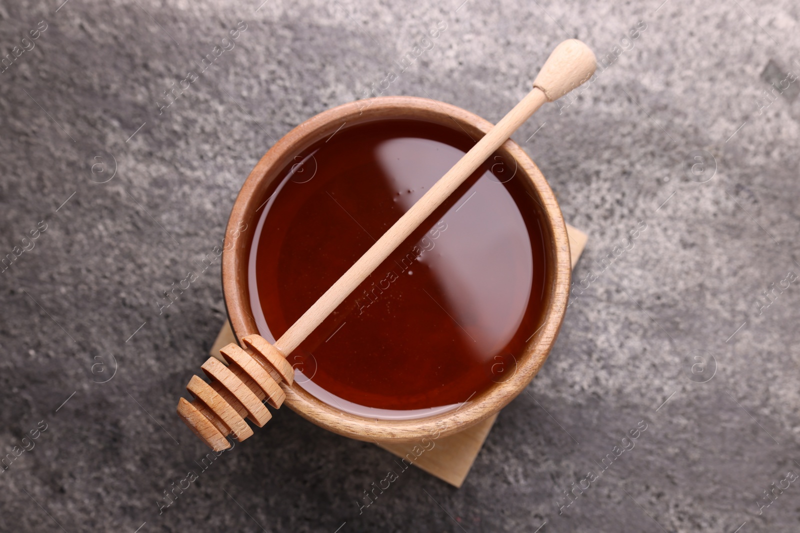 Photo of Delicious honey in bowl and dipper on grey textured table, top view