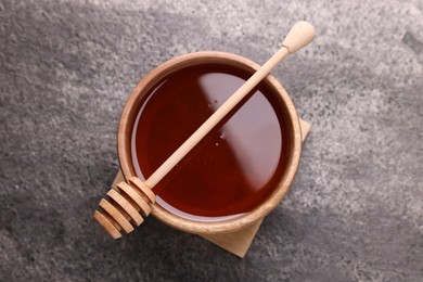 Photo of Delicious honey in bowl and dipper on grey textured table, top view