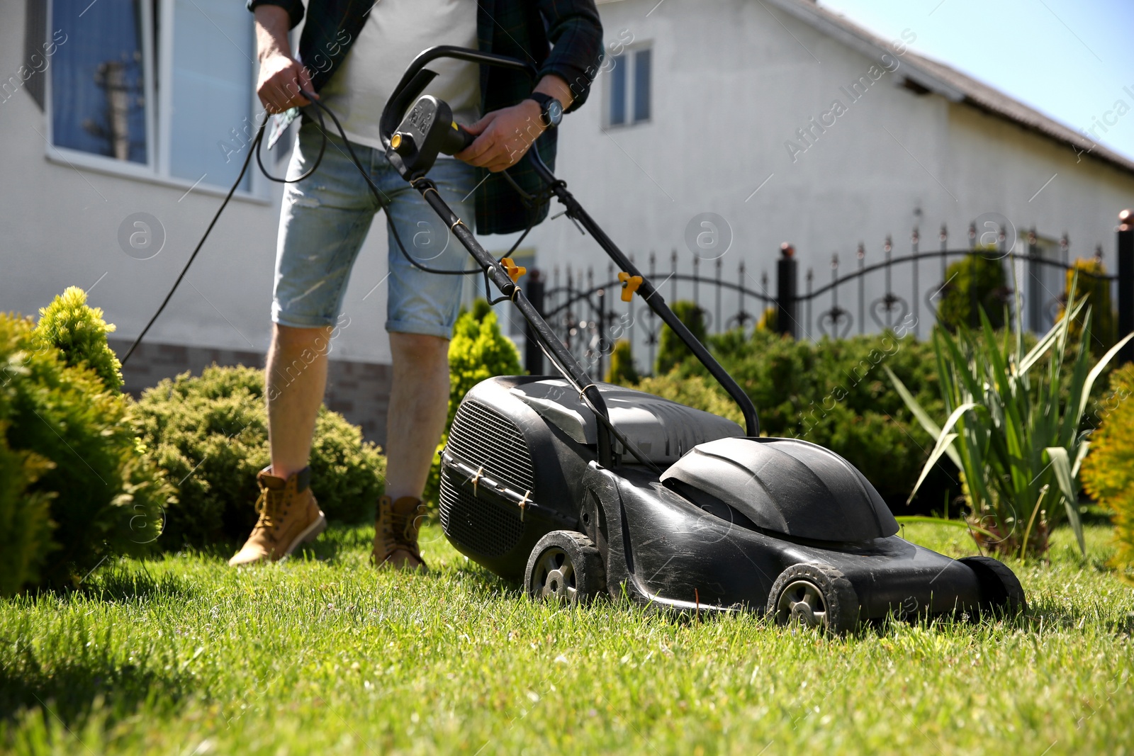 Photo of Man cutting green grass with lawn mower in garden, closeup