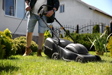 Photo of Man cutting green grass with lawn mower in garden, closeup