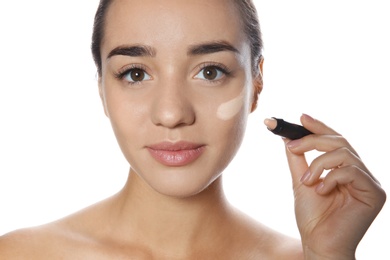 Young woman applying foundation on her face against white background