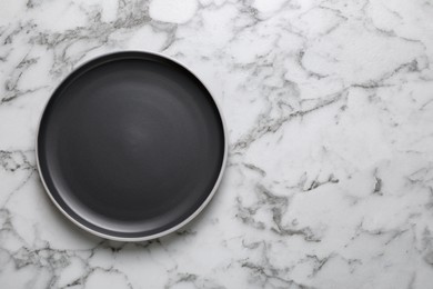 Photo of New dark plate on white marble table, top view. Space for text