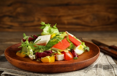 Photo of Delicious salad with crab sticks and lettuce on wooden plate, closeup