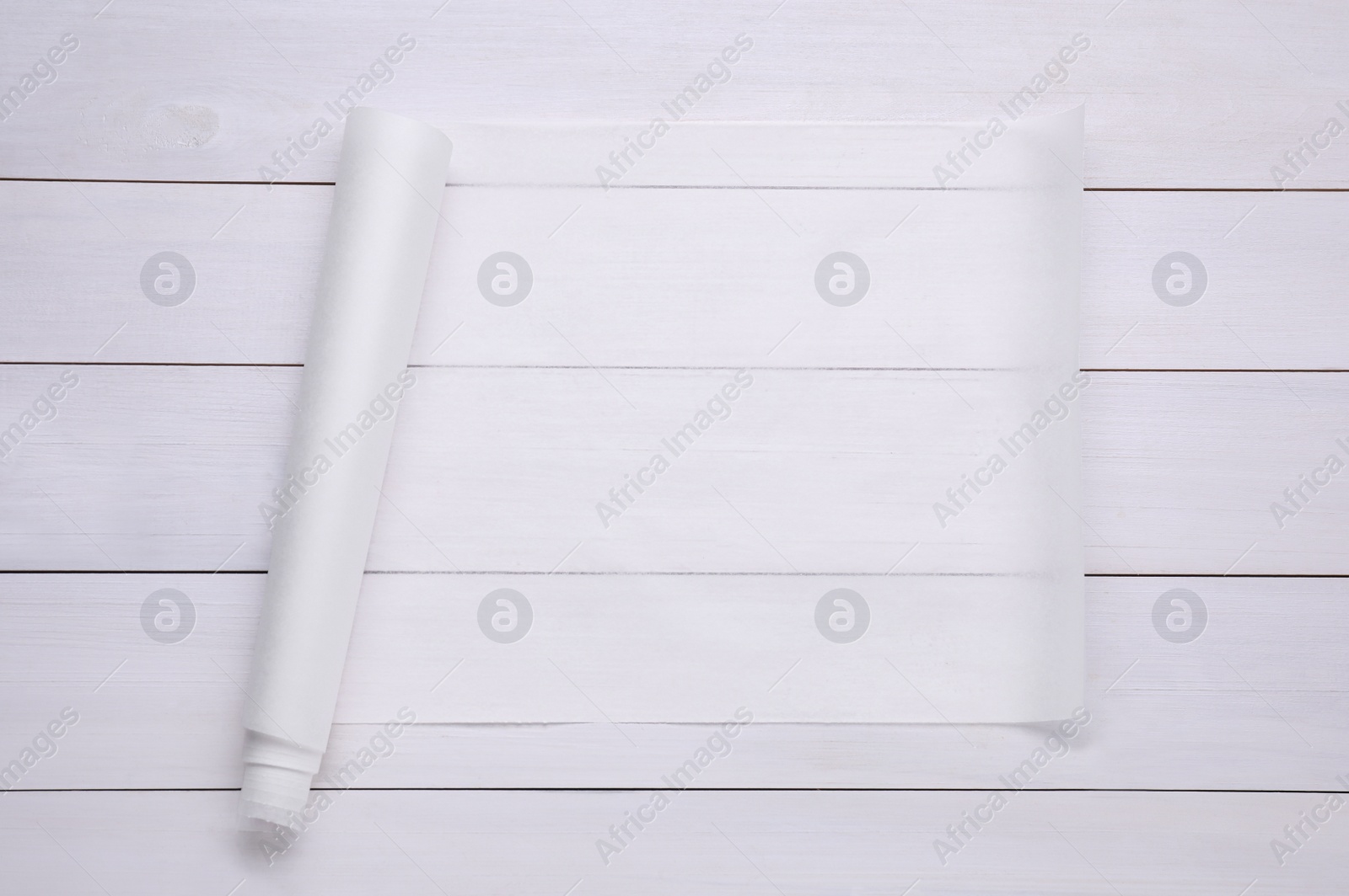 Photo of Roll of baking paper on white wooden table, top view