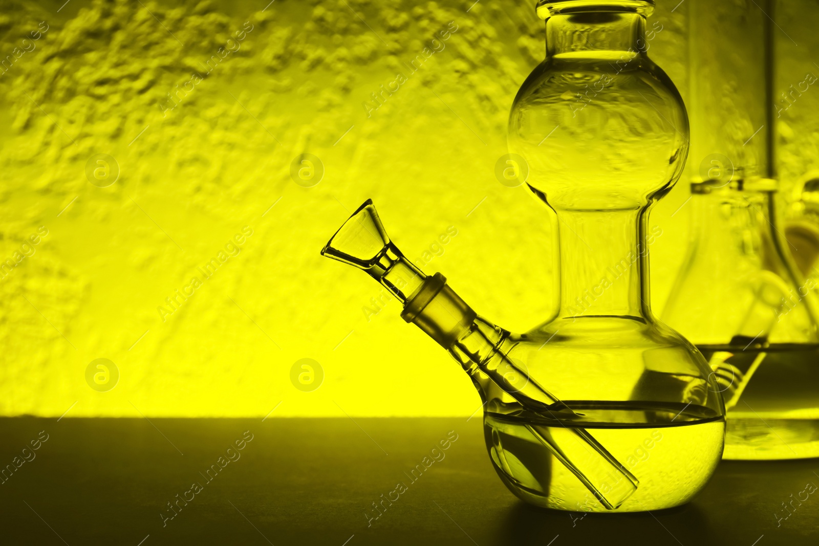 Photo of Closeup view of glass bong on table, space for text. Smoking device