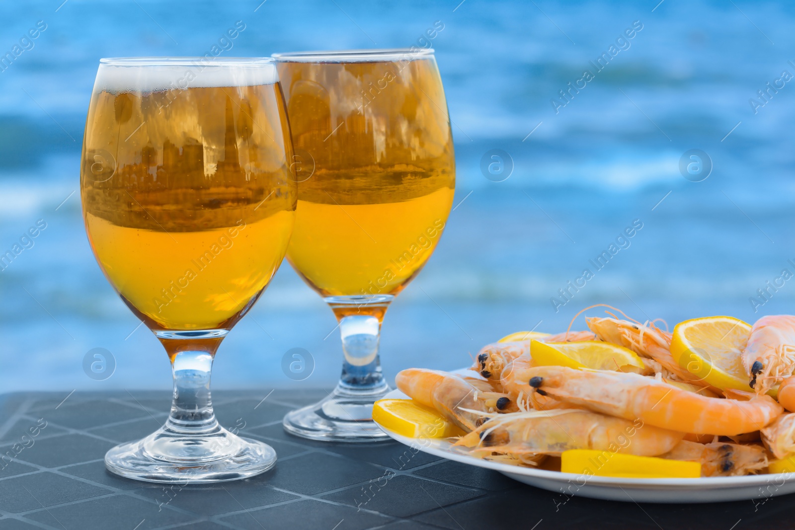 Photo of Cold beer in glasses and shrimps served with lemon on beach, closeup