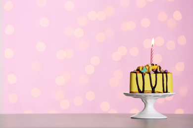 Photo of Piece of delicious birthday cake with burning candle on table against festive lights. Space for text