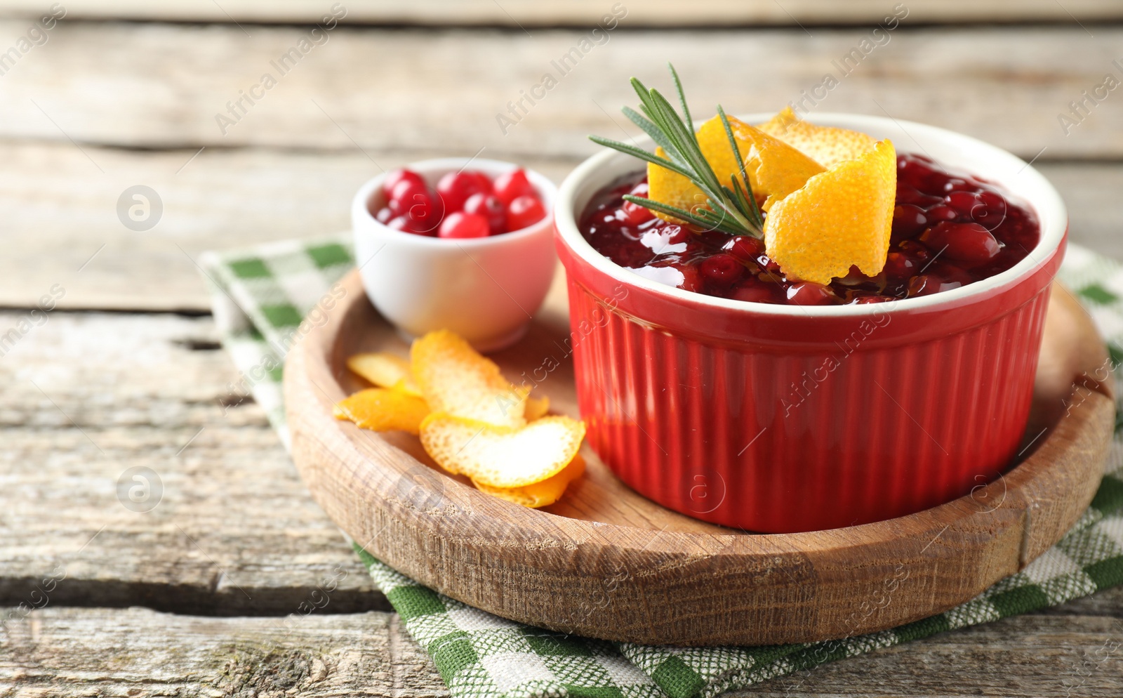 Photo of Cranberry sauce in bowl, fresh berries, rosemary and orange peels on wooden table, closeup. Space for text