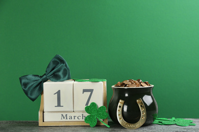 Photo of Composition with pot of gold coins and wooden block calendar on grey stone table against green background. St. Patrick's Day celebration