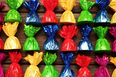 Photo of Many candies in colorful wrappers on wooden table, flat lay