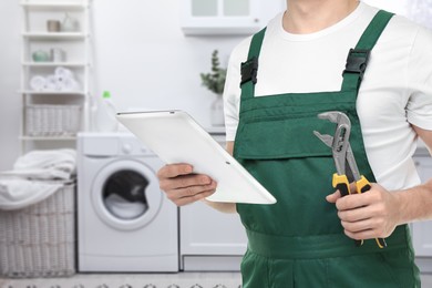 Image of Plumber with pipe wrench and tablet in bathroom, closeup. Space for text