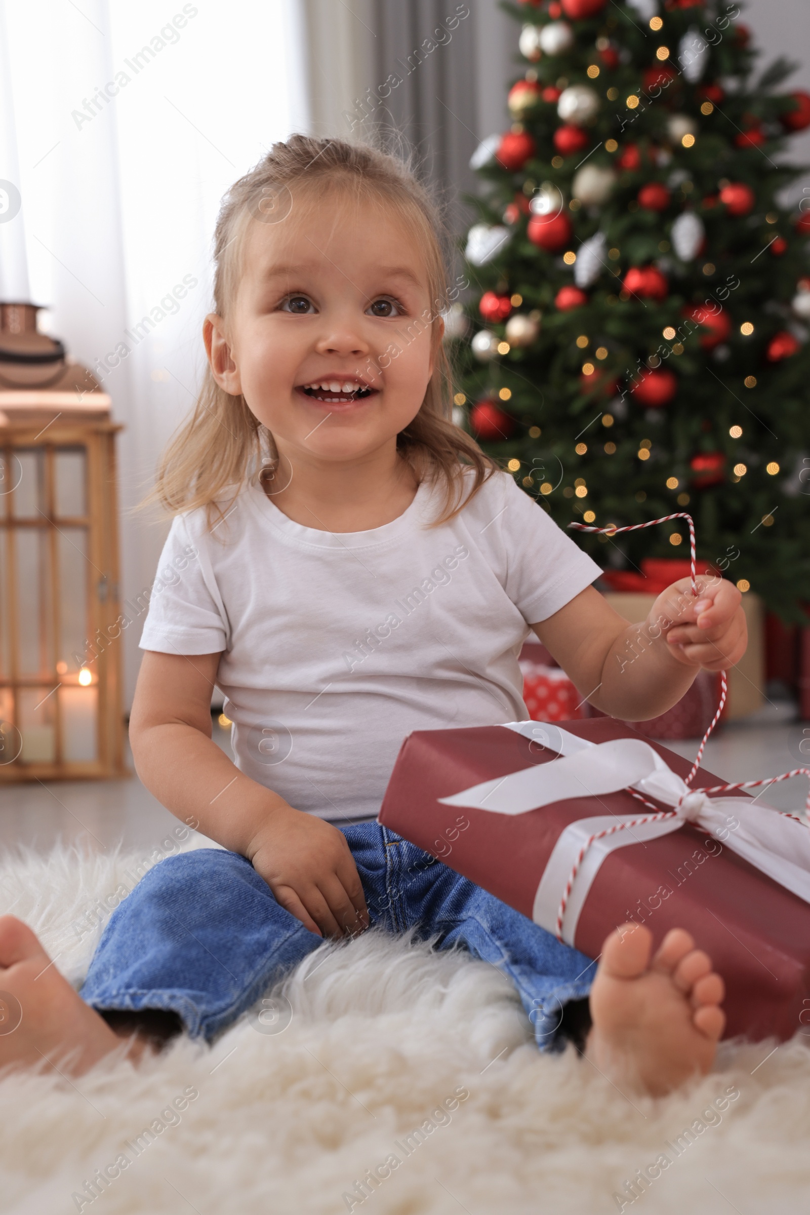 Photo of Cute little girl with Christmas gift in festively decorated room