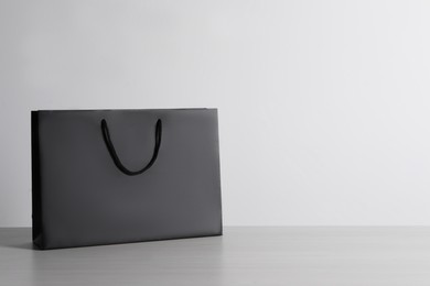 Photo of Black paper bag on white wooden table, space for text