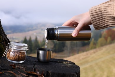 Photo of Woman pouring hot water into cup with instant coffee in mountains, closeup