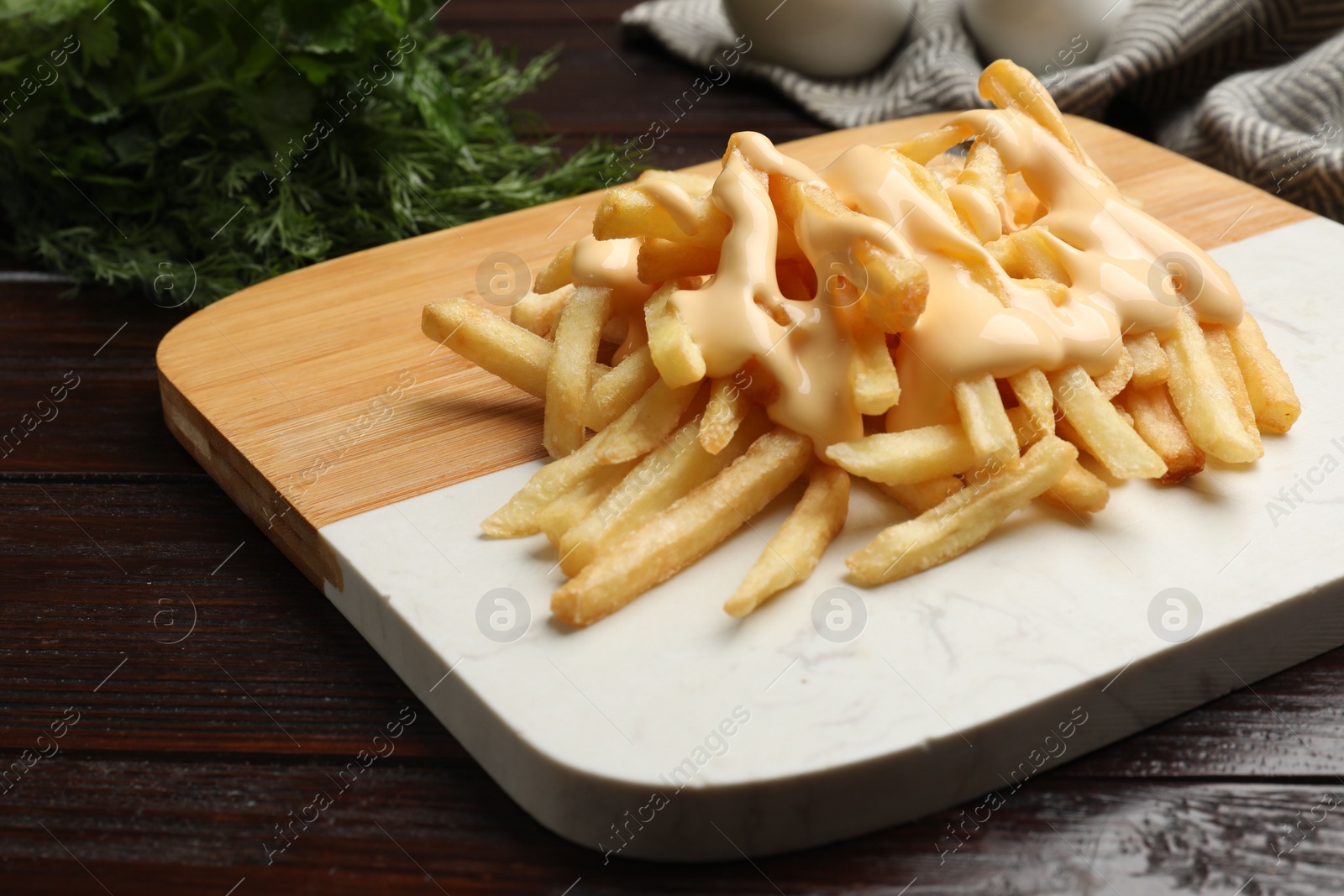 Photo of Delicious french fries with cheese sauce on wooden table, closeup