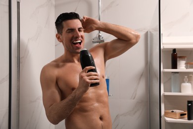Photo of Man with bottle of gel singing in shower at home