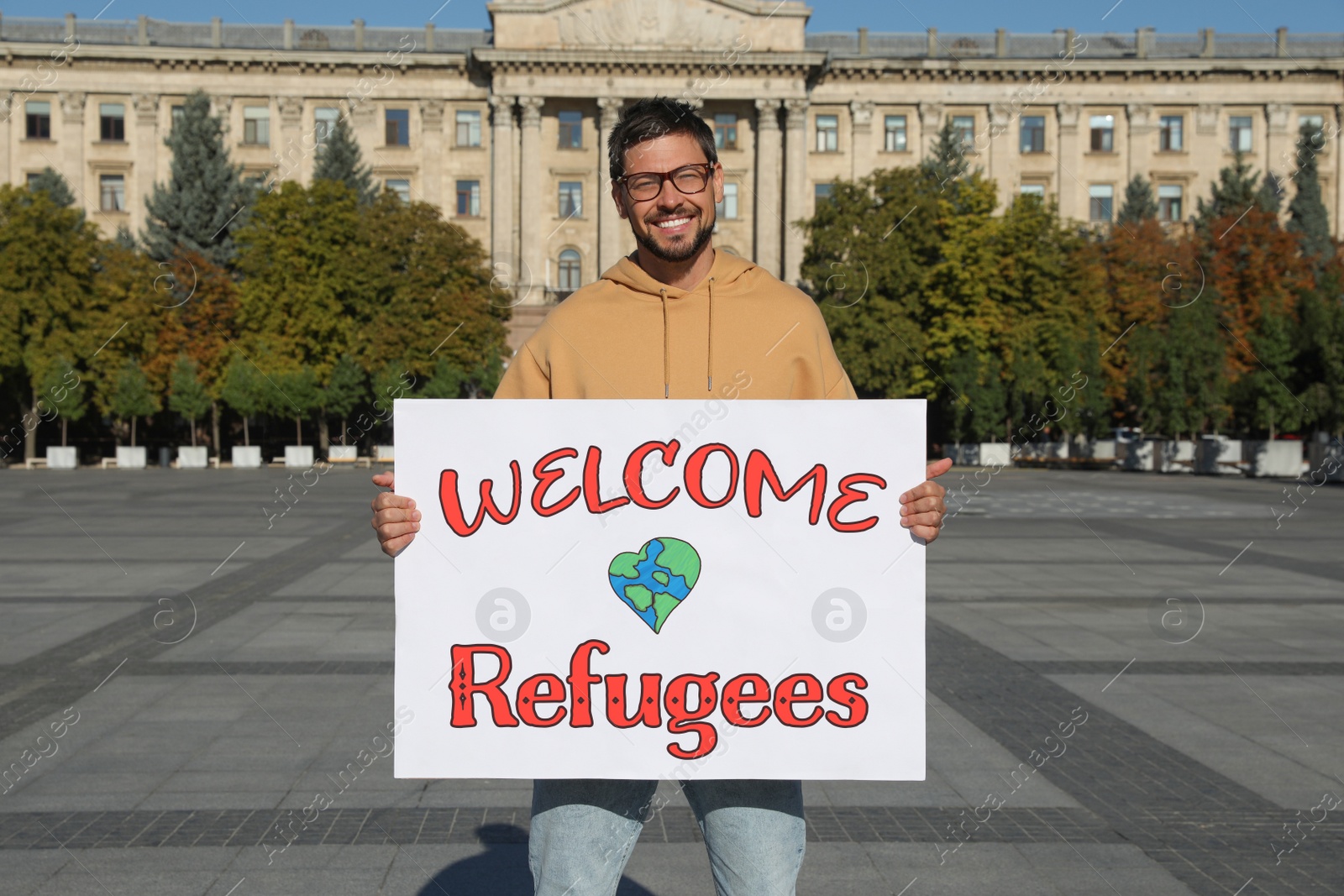 Image of Man holding poster with phrase WELCOME REFUGEES on city street