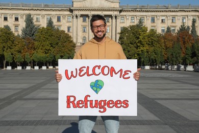 Man holding poster with phrase WELCOME REFUGEES on city street