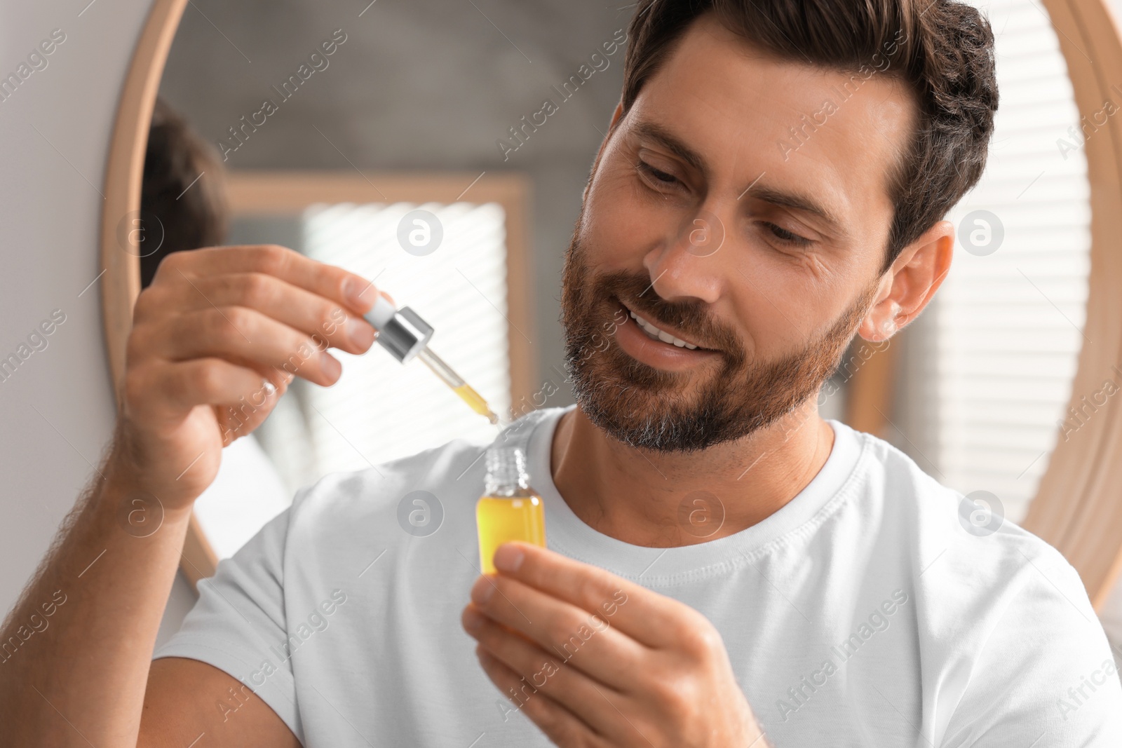 Photo of Smiling man with bottle of cosmetic serum indoors