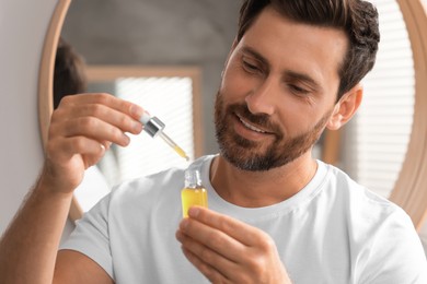 Photo of Smiling man with bottle of cosmetic serum indoors