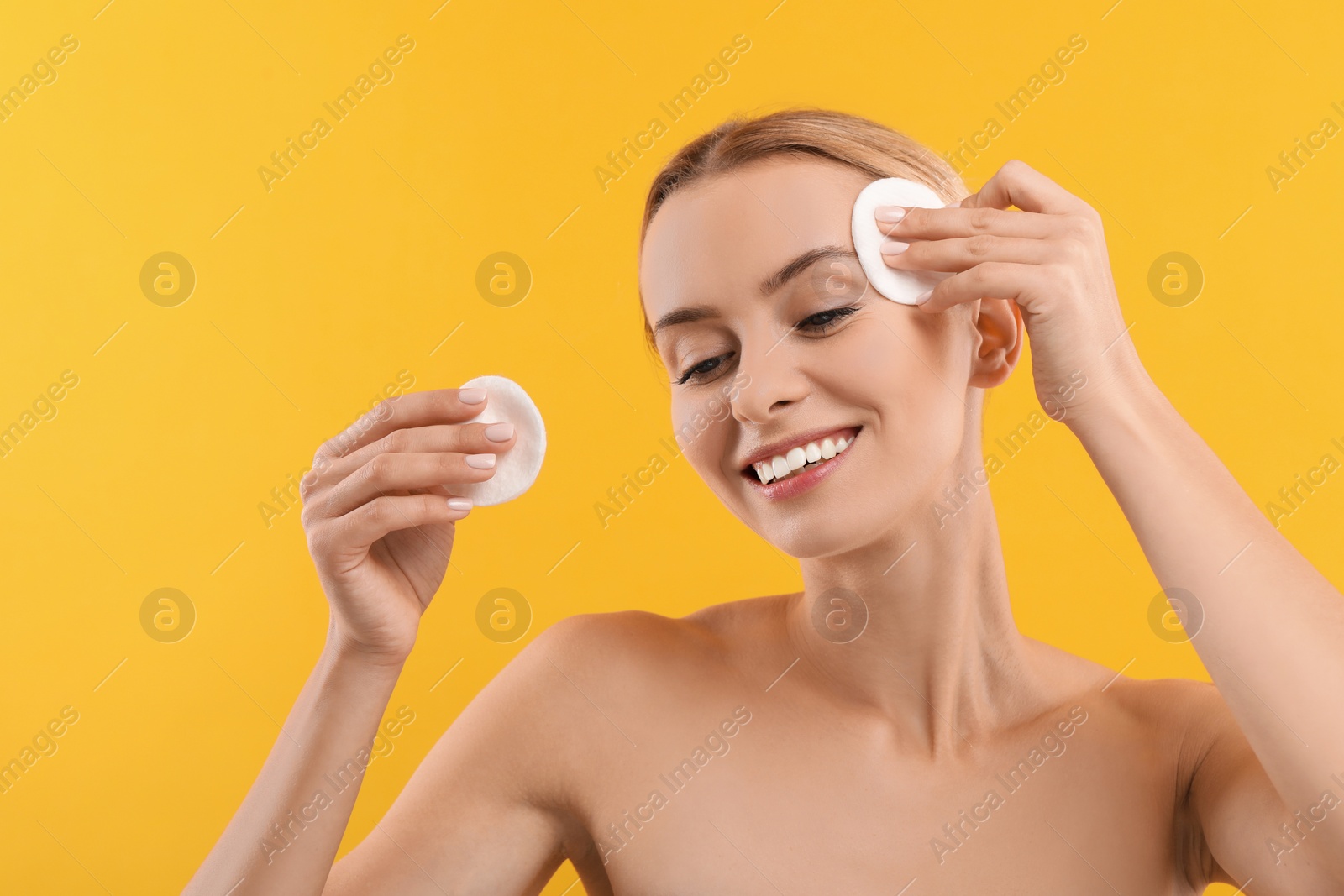 Photo of Smiling woman removing makeup with cotton pads on yellow background