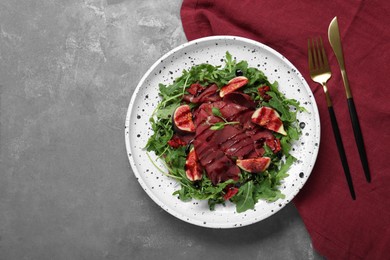 Photo of Plate of tasty bresaola salad with figs, sun-dried tomatoes, balsamic vinegar and cutlery on grey table, flat lay. Space for text