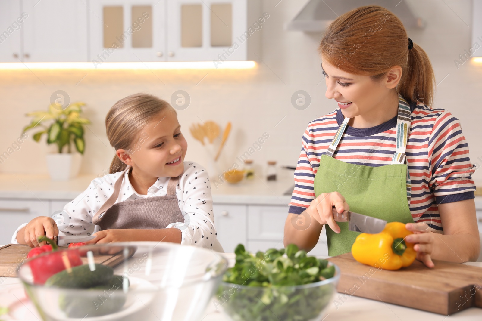 Photo of Mother and daughter cooking salad together in kitchen