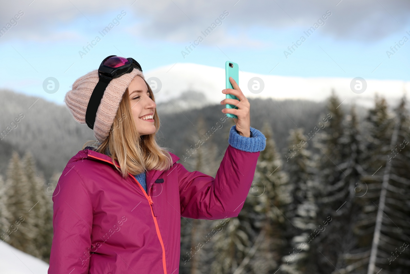 Photo of Young woman with ski goggles using smartphone in mountains during winter vacation. Space for text