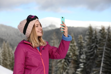 Young woman with ski goggles using smartphone in mountains during winter vacation. Space for text