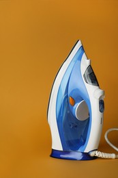 Photo of One modern iron on orange background. Home appliance