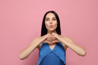 Photo of Beautiful young woman blowing kiss and making heart with hands on pink background