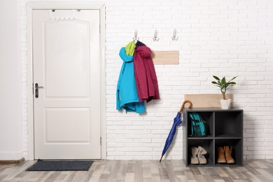 Stylish hallway interior with shoe rack and hanging clothes on brick wall