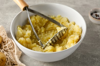 Bowl with delicious mashed potato and masher on light grey table, closeup