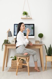 Young woman with cup of drink at table in room. Home office