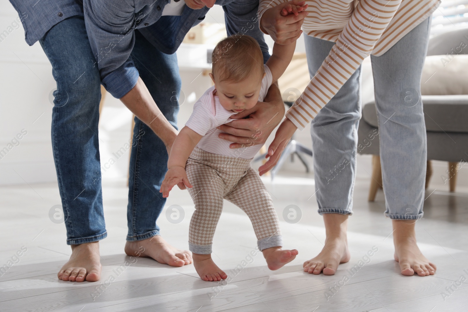 Photo of Parents supporting their baby daughter while she learning to walk at home