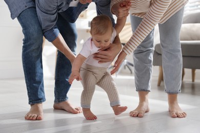 Parents supporting their baby daughter while she learning to walk at home