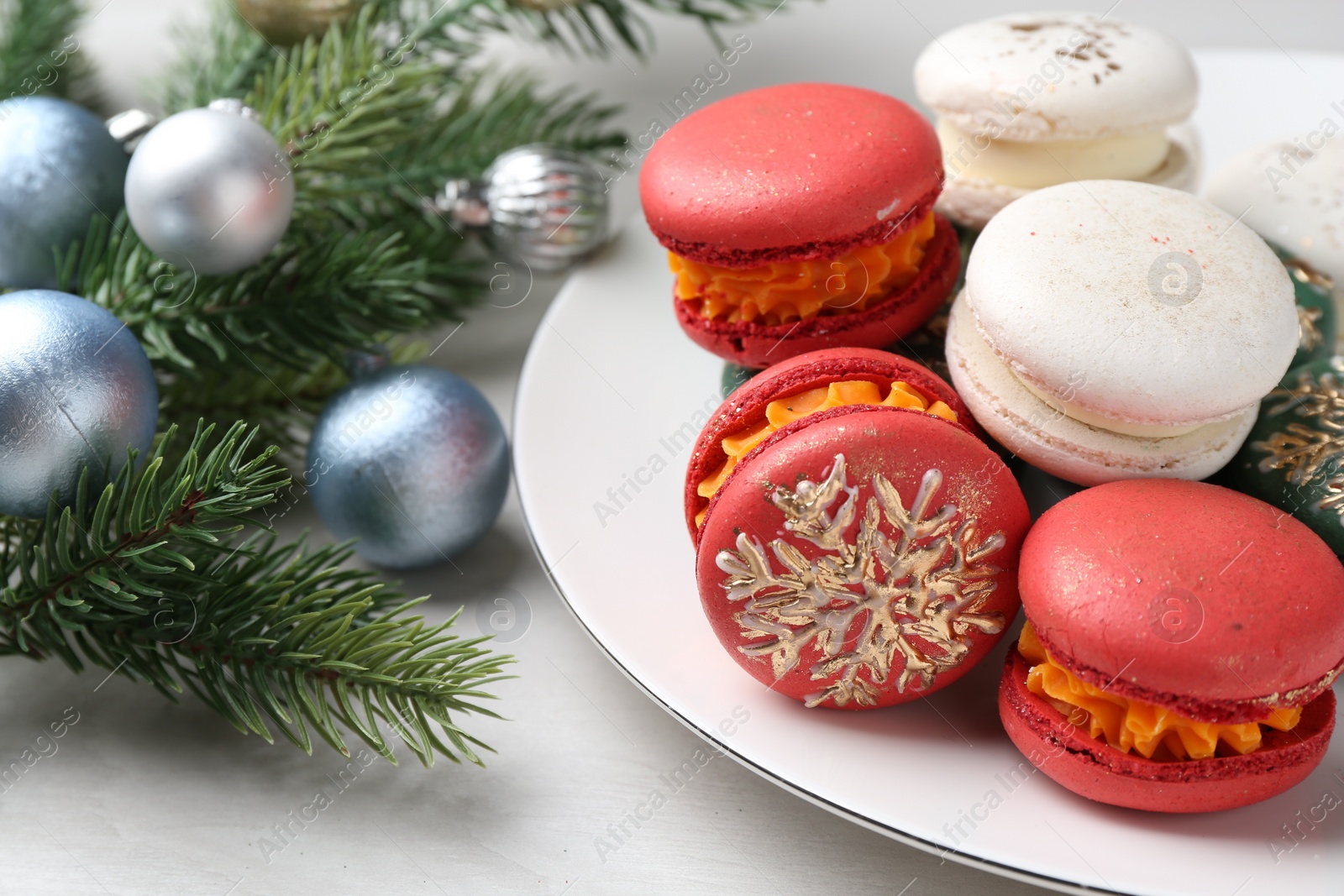 Photo of Different decorated Christmas macarons and festive decor on white wooden table