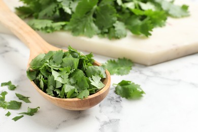 Photo of Cut fresh green cilantro and wooden spoon on white marble table, closeup. Space for text
