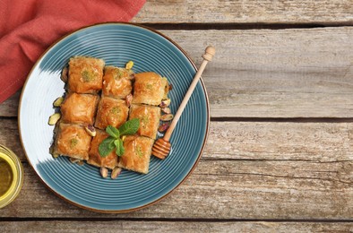 Photo of Delicious baklava with pistachios, honey and mint on wooden table, flat lay. Space for text