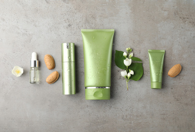 Photo of Set of cosmetic products, almond nuts and flowers on grey table, flat lay