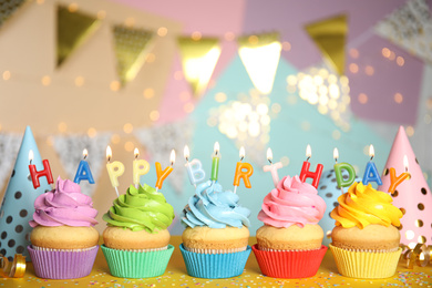 Birthday cupcakes with burning candles on yellow table