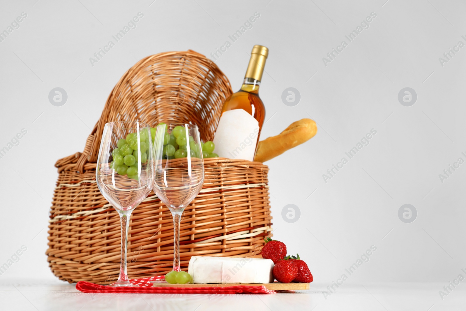 Photo of Picnic basket with wine, glasses and products on white background