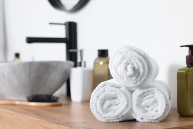 Photo of Rolled bath towels on wooden table in bathroom. Space for text