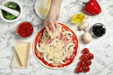 Photo of Woman adding grated cheese to unbaked pizza on marble table, top view