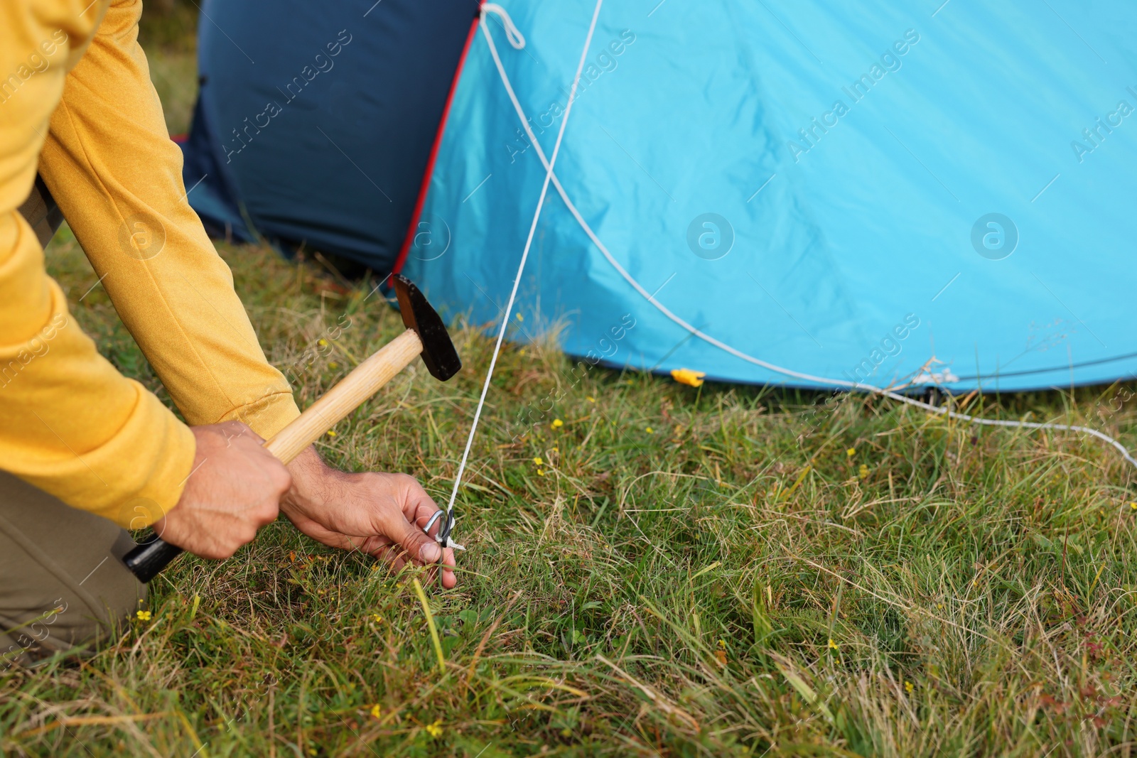 Photo of Man setting up camping tent outdoors, closeup