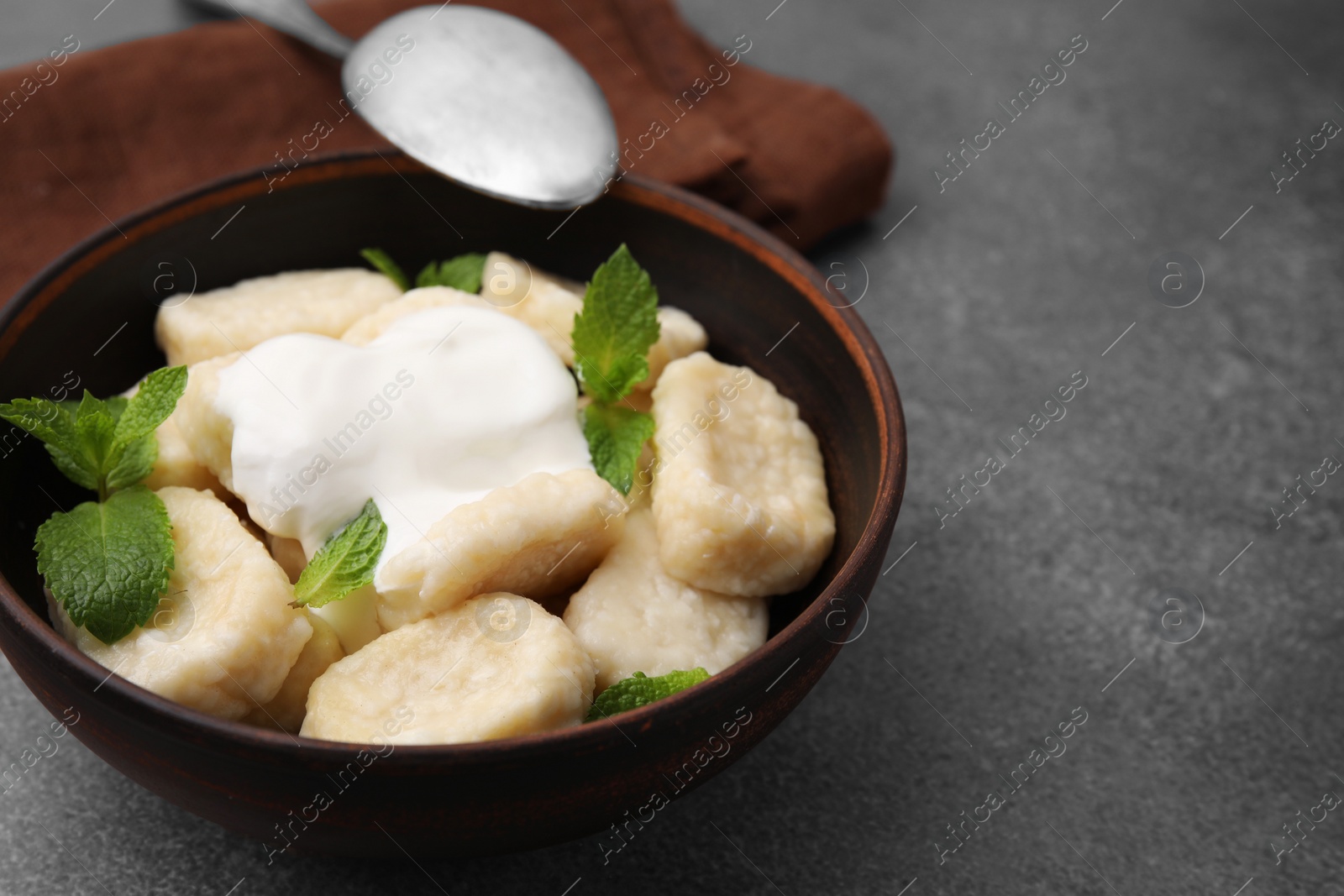 Photo of Bowl of tasty lazy dumplings with sour cream and mint leaves on brown table. Space for text